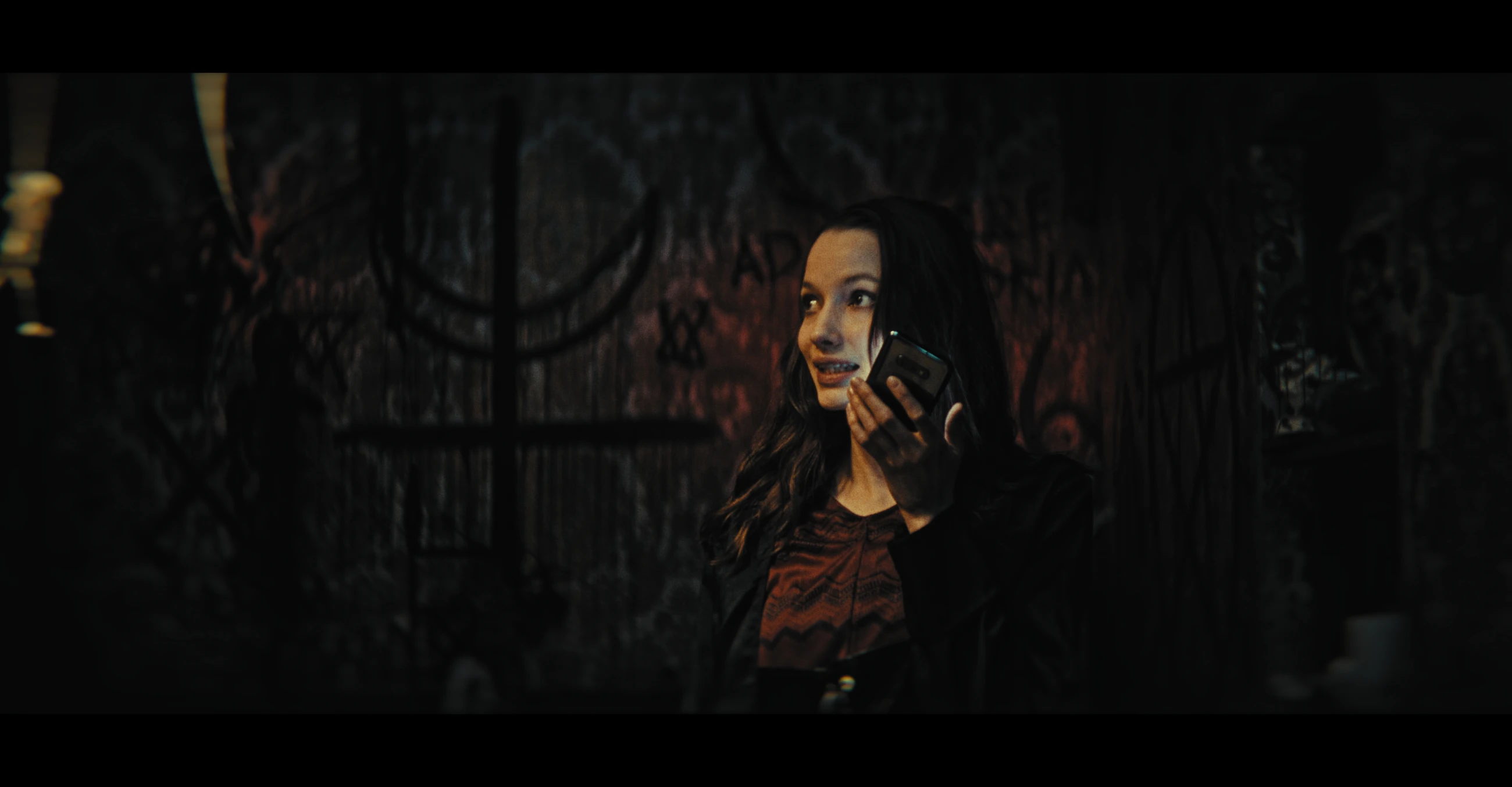 A woman holds a phone in a dim, graffiti-covered room in The Maze.