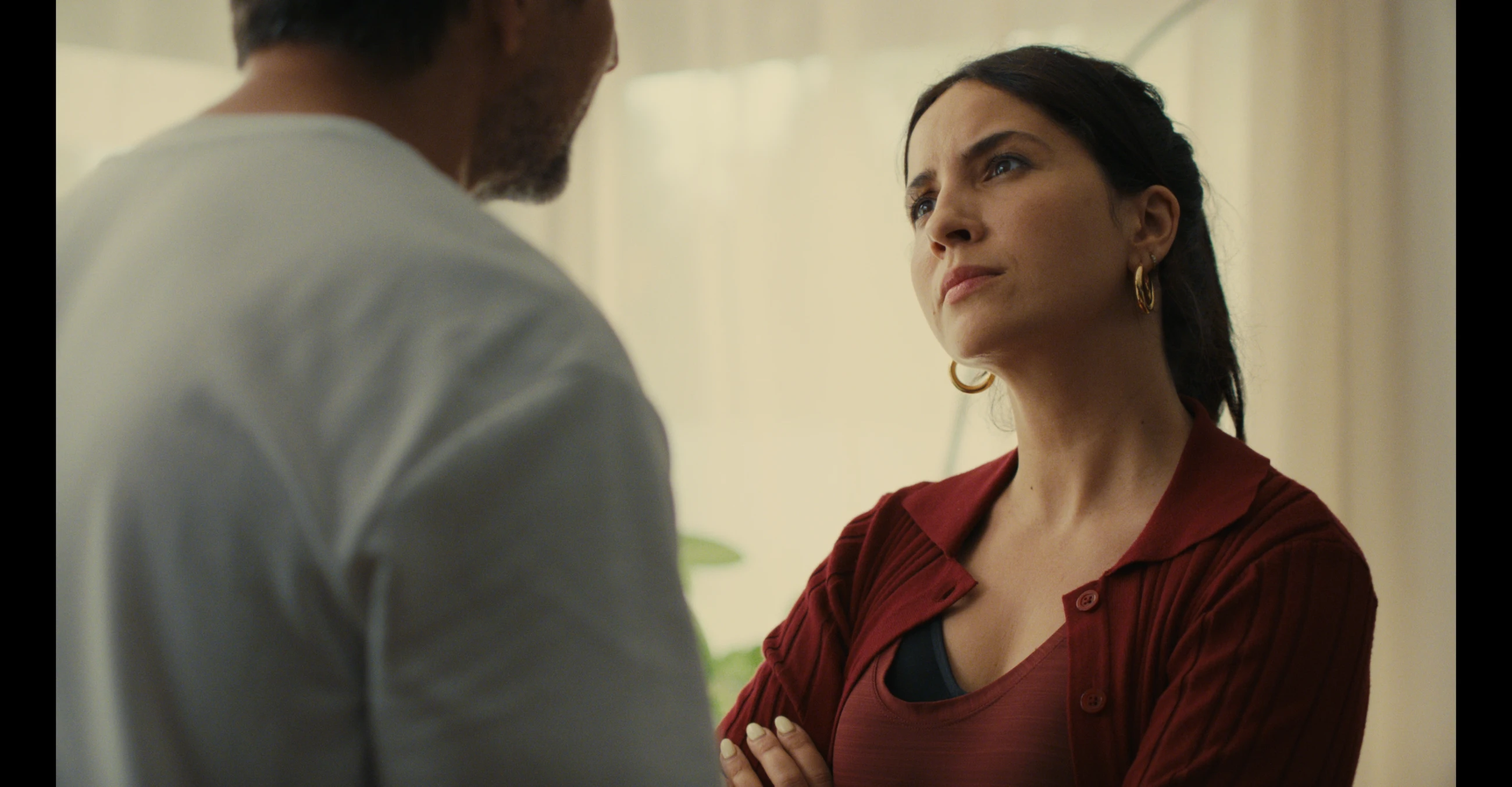 A woman with folded arms faces a man in a bright room in The Other gAIrl.
