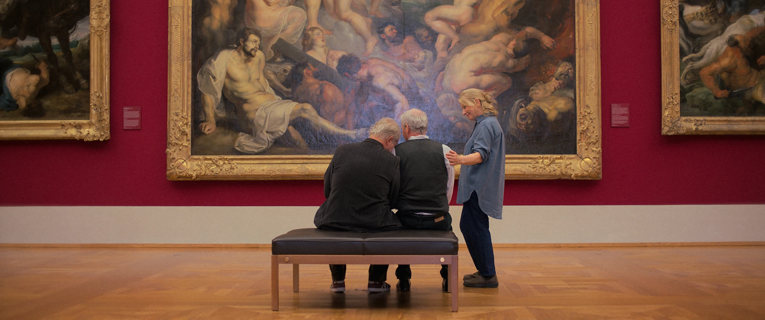 Two museum visitors and a guide stand before a large painting in Der verlorene Mann.