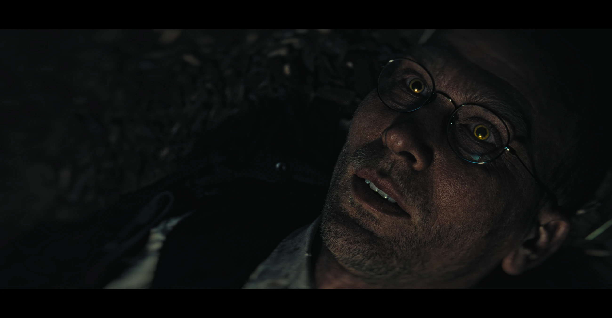 Close-up of a man with round glasses lying in darkness in The Maze.