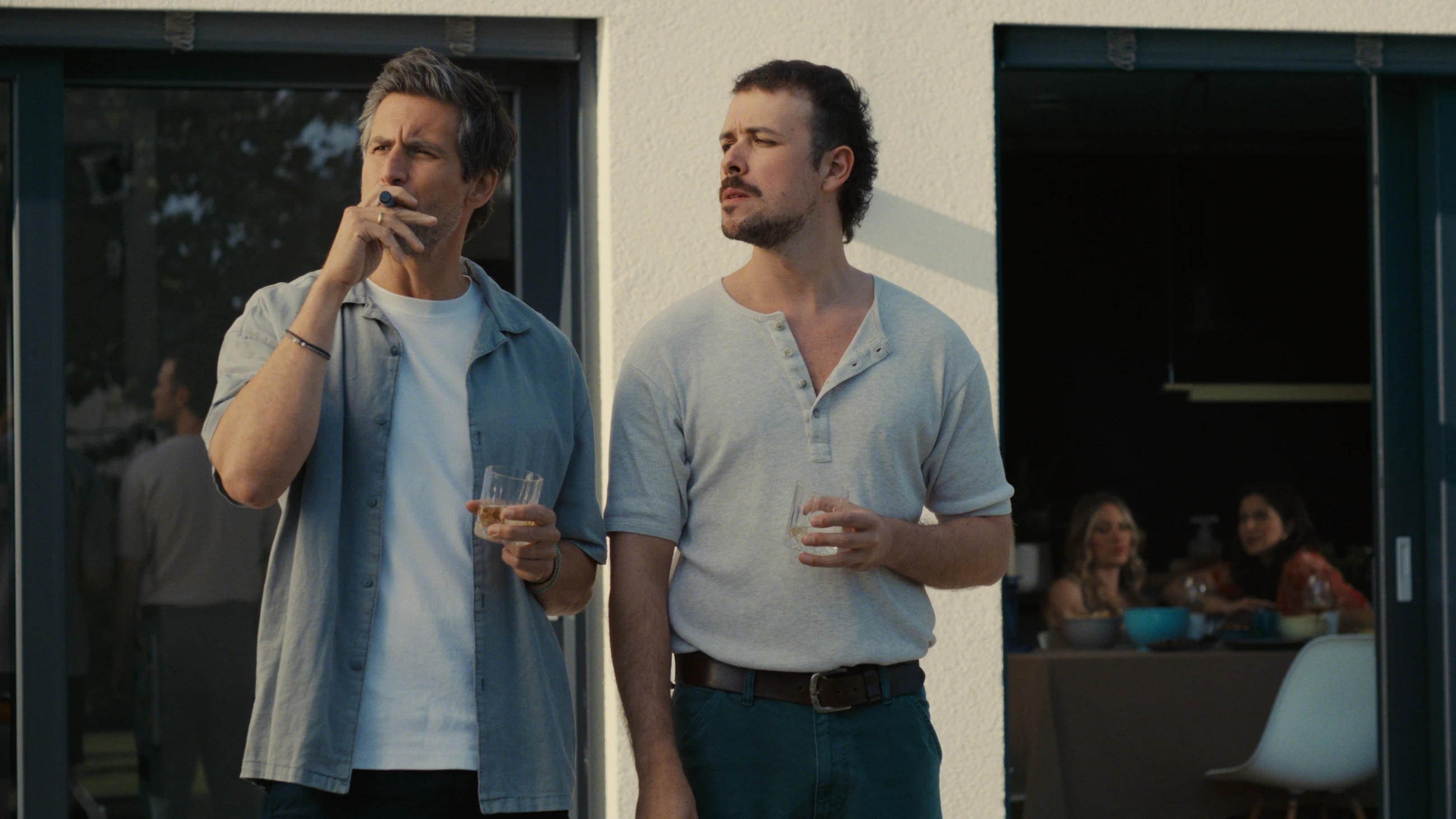 Two men stand outside with drinks during a family gathering in The Other gAIrl.